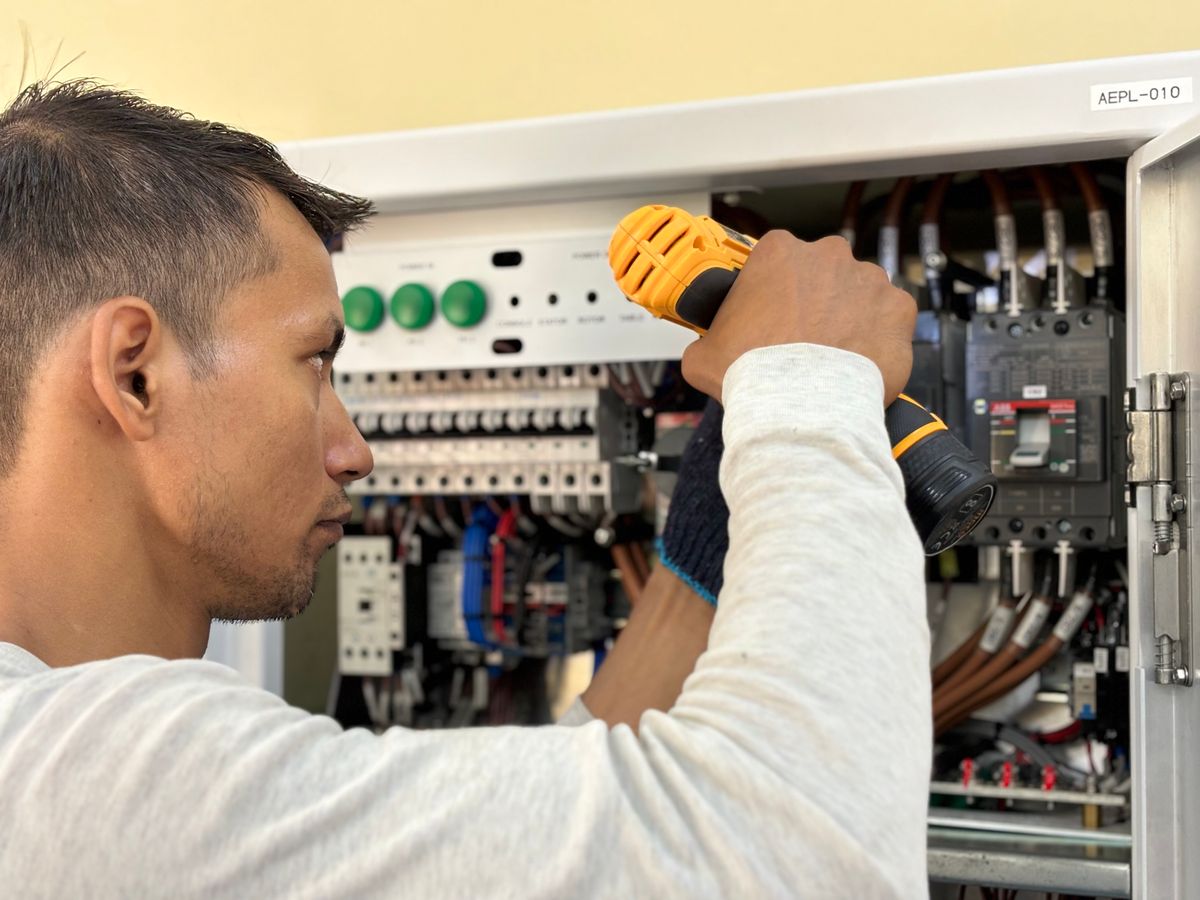 Elektriker arbeitet mit Bohrmaschine an einem geöffneten Sicherungskasten