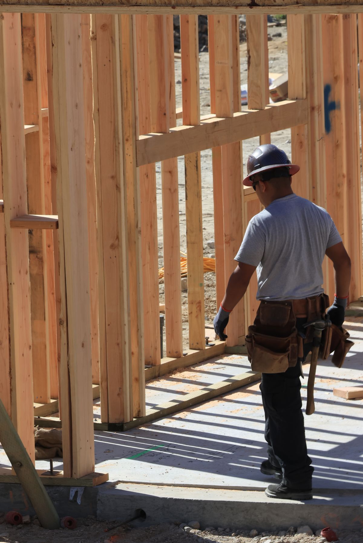 Handwerker mit Werkzeuggürtel und Schutzhelm beim Aufbau eines Wohnhauses
