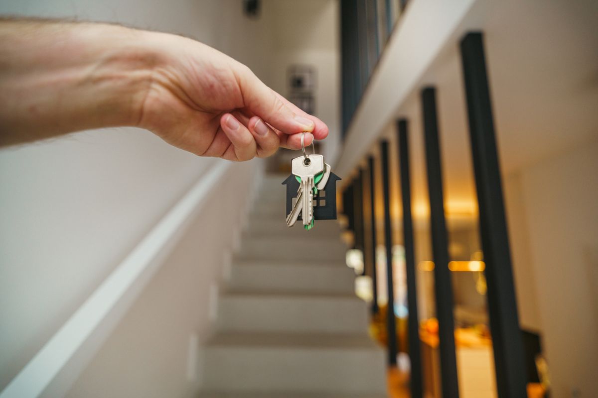 Hand hält einen Wohnungsschlüssel vor einer modernen Haustür nach erfolgreicher Türöffnung