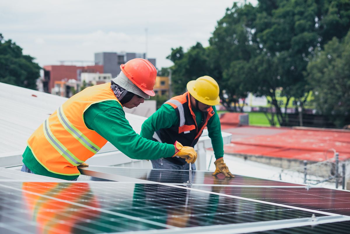 Zwei Solartechniker montieren gemeinsam Photovoltaik-Module auf einem Dach