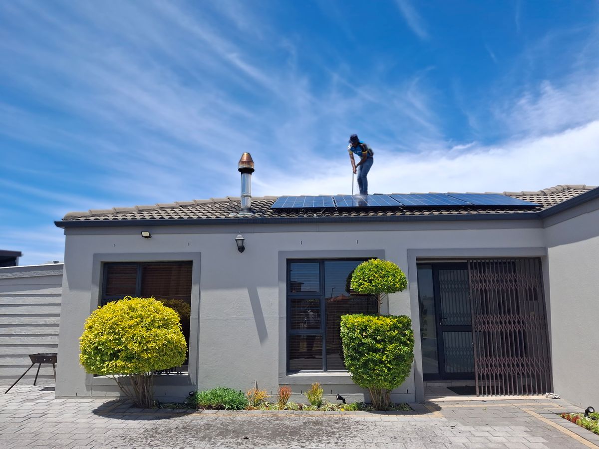 Handwerker installiert Photovoltaik-Module auf einem Wohnhausdach bei klarem Himmel