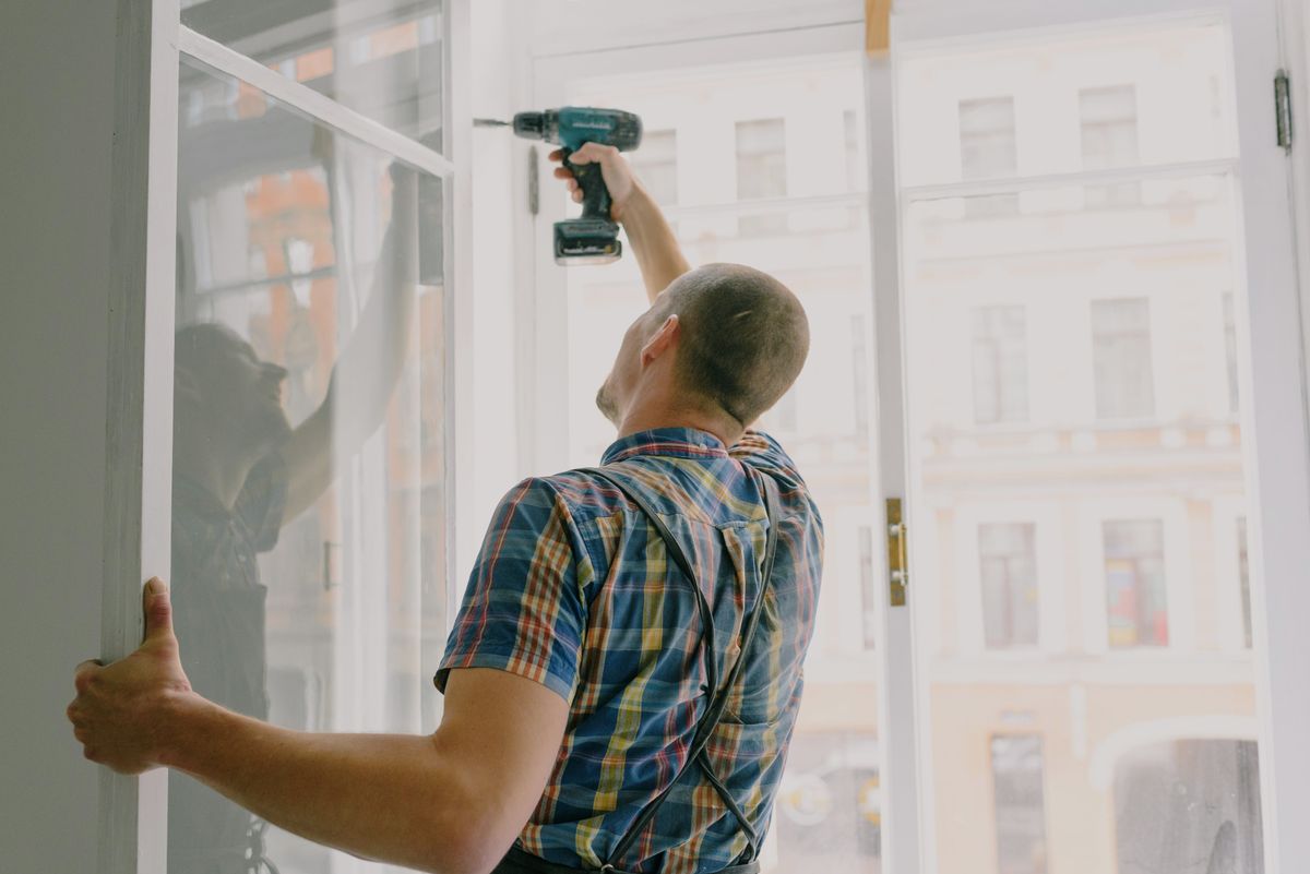 Handwerker montiert einen neuen Fensterrahmen mit Bohrmaschine im Innenraum
